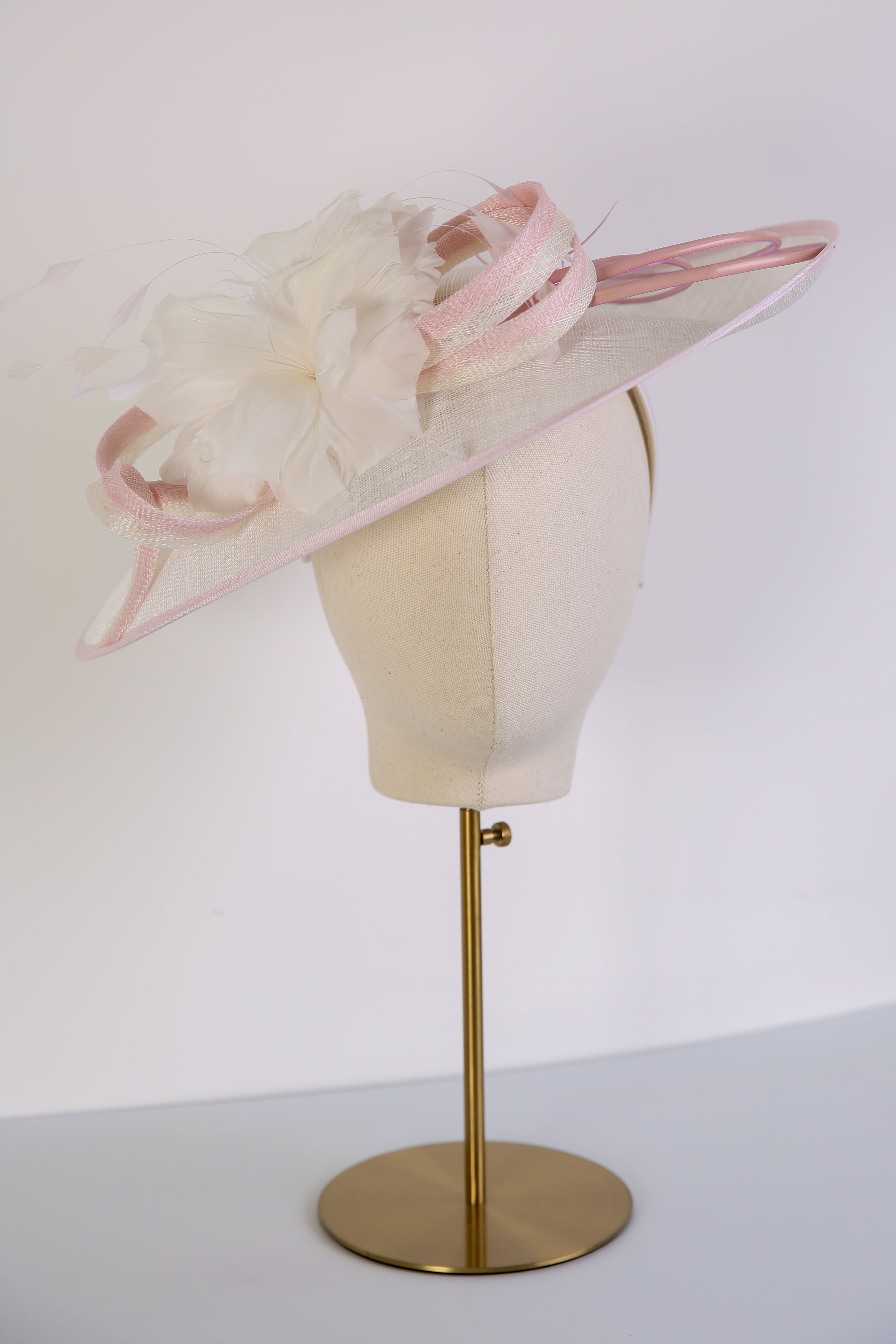 Pink and white decorative hat on a mannequin head with a white background