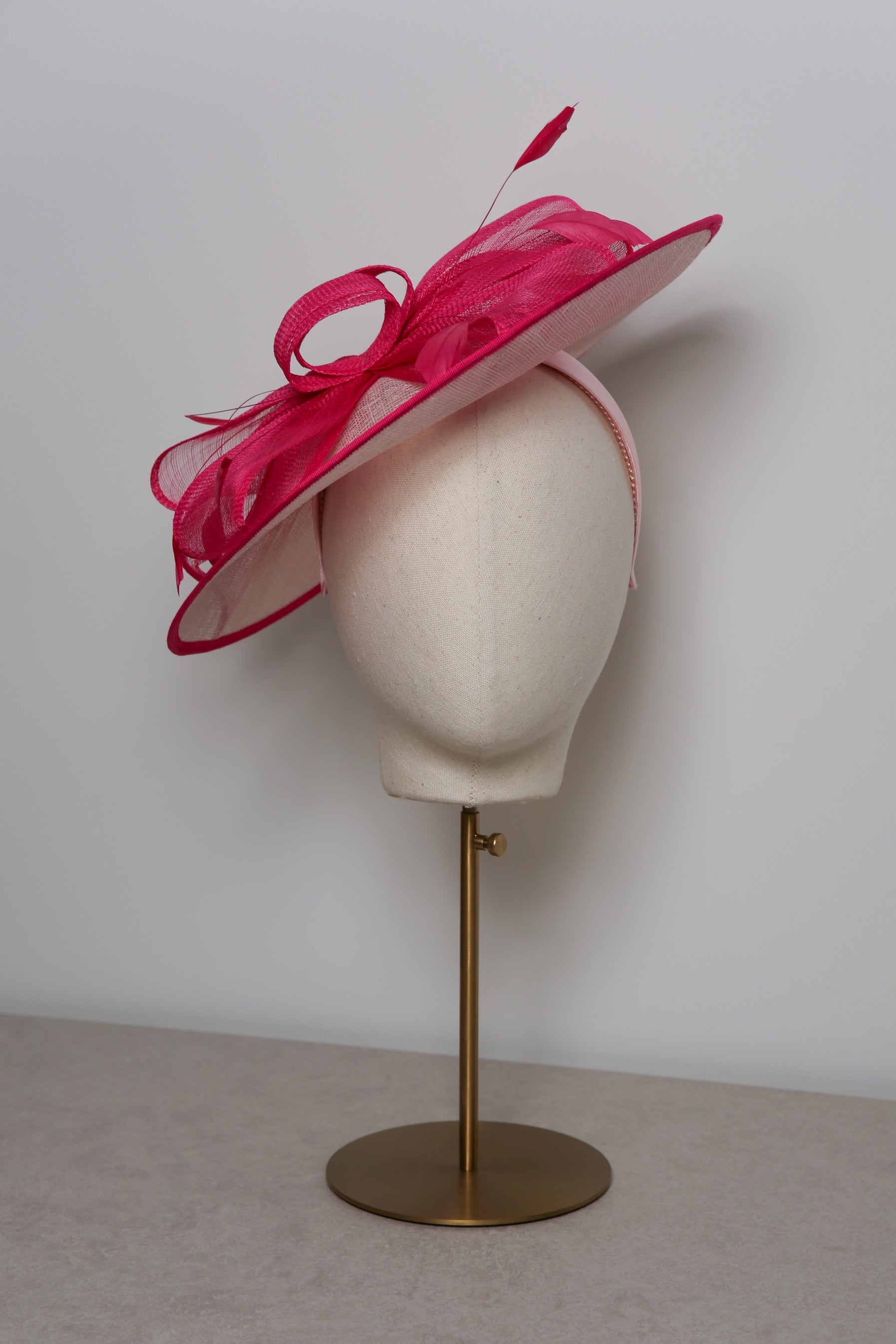 Pink and white hat with a large bow on a mannequin head against a white background