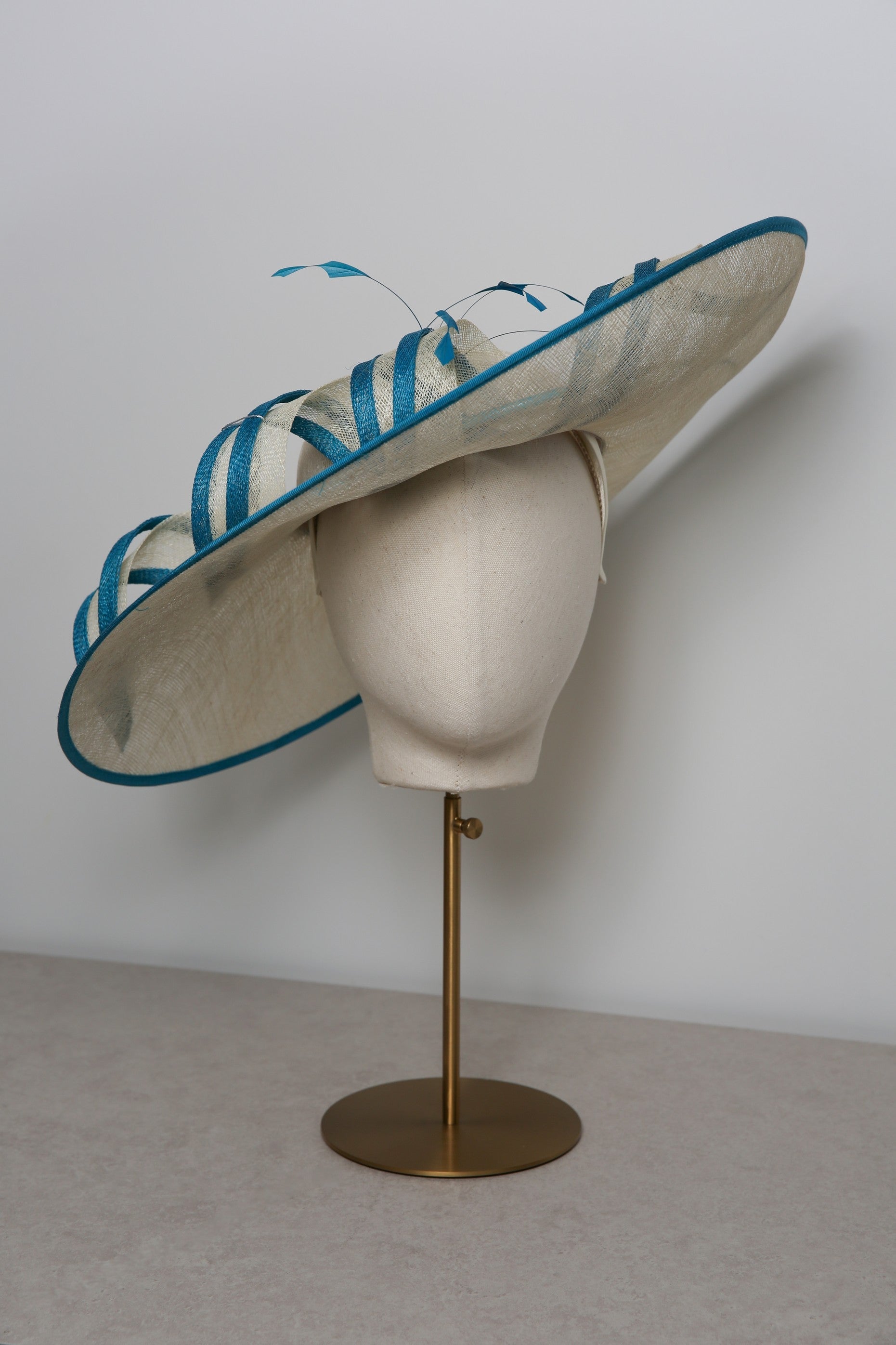 Large decorative hat with blue accents on a mannequin head against a plain background