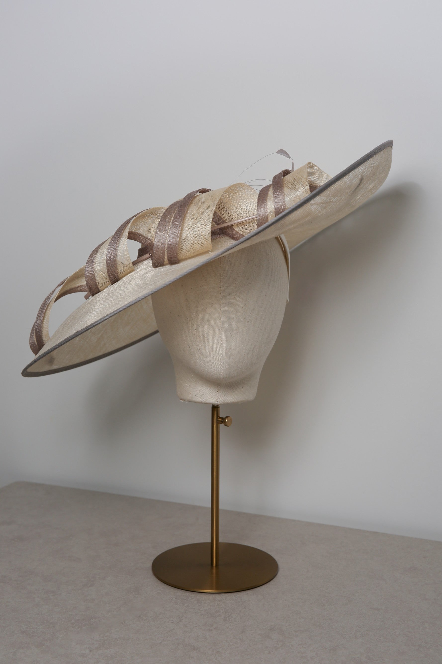 Large decorative hat on a mannequin head with a plain background