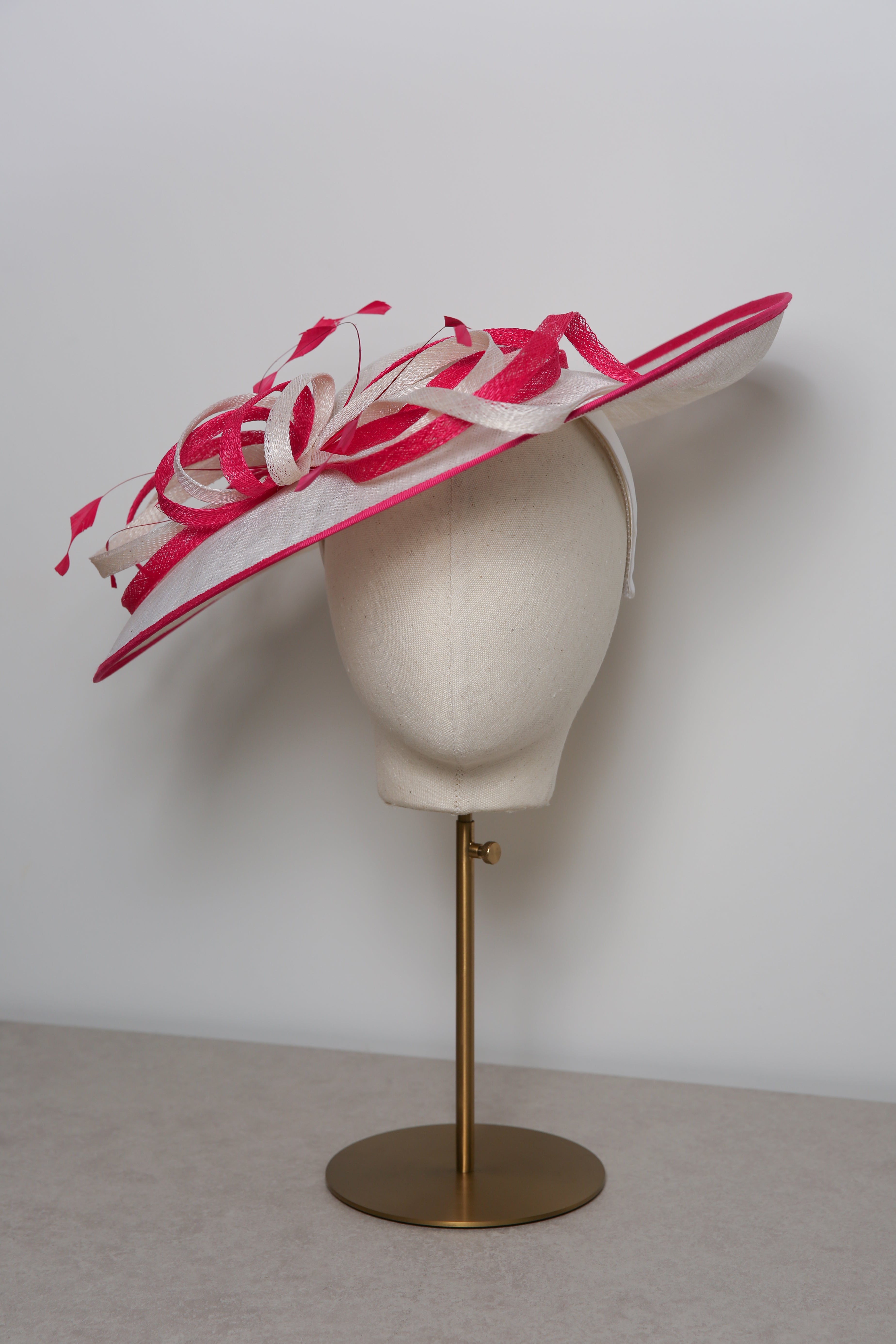 Pink and white decorative hat on a mannequin head against a plain background