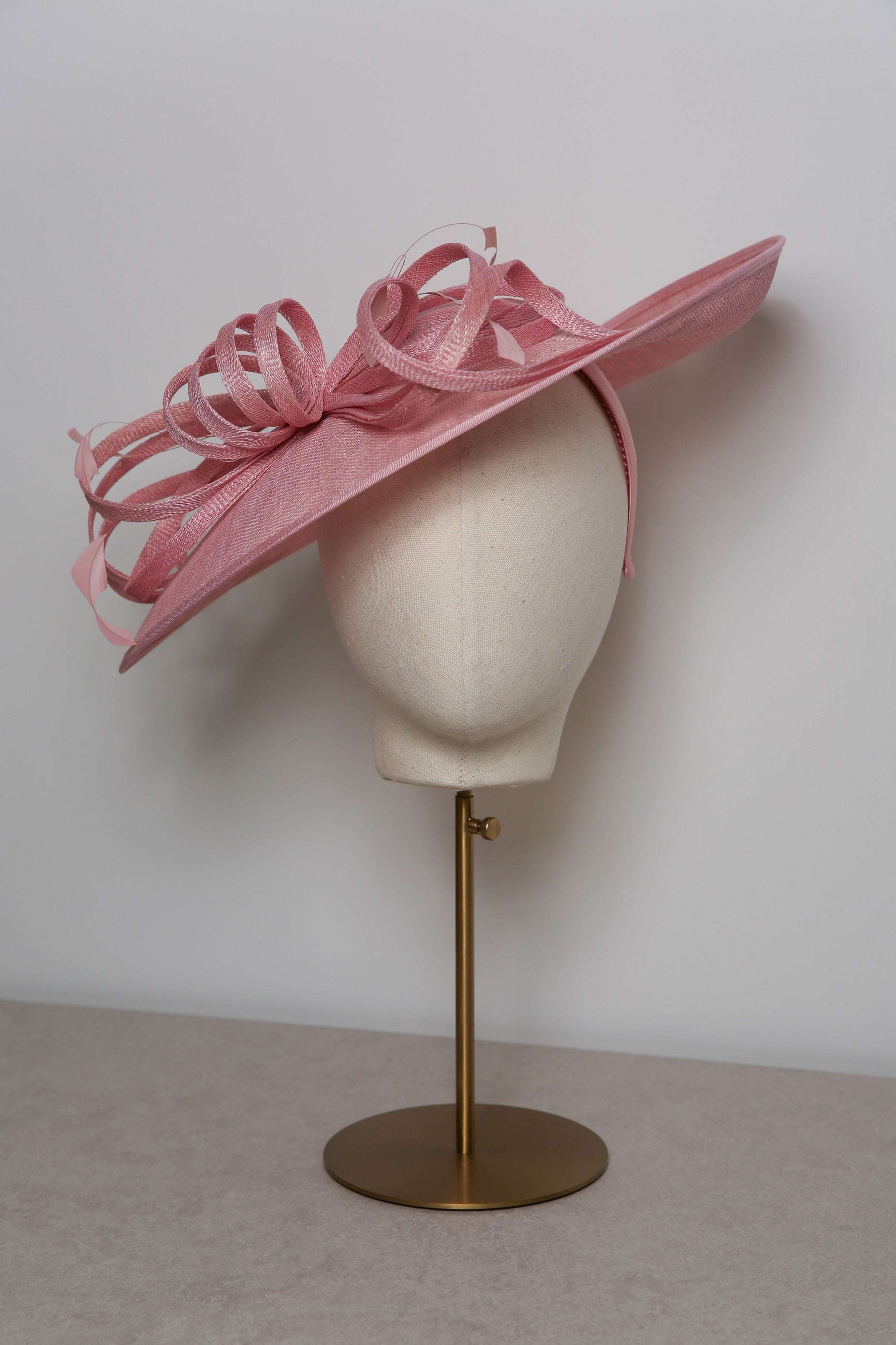 Pink decorative hat on a mannequin head against a plain background