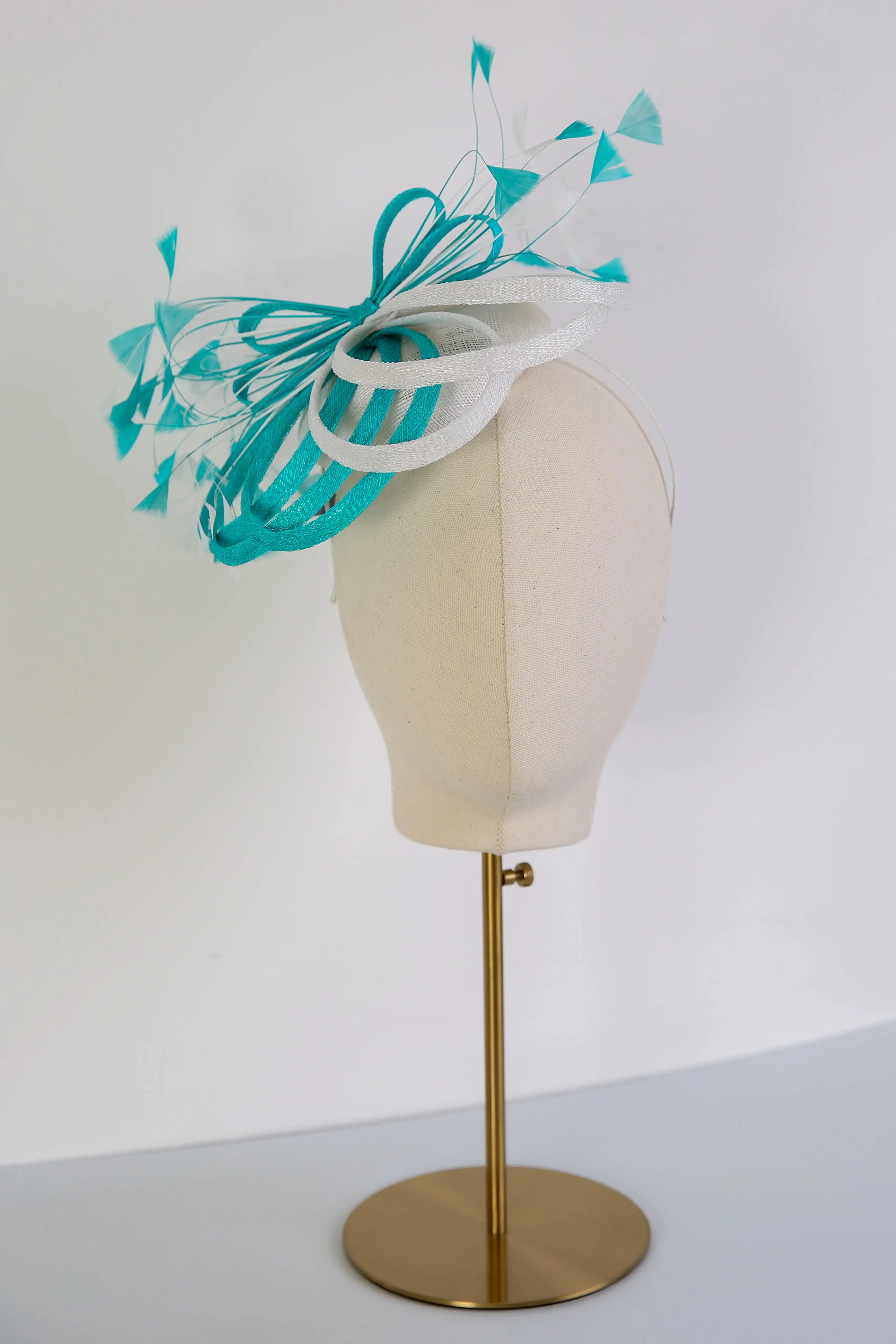Teal and white decorative headpiece on a mannequin head against a white background